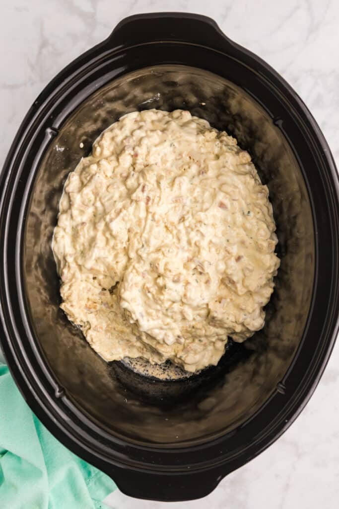 Uncooked casserole mixture spread in a slow cooker.