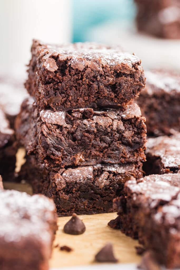 Three thick chocolate brownies stacked vertically, each with a crackly top and powdered sugar.