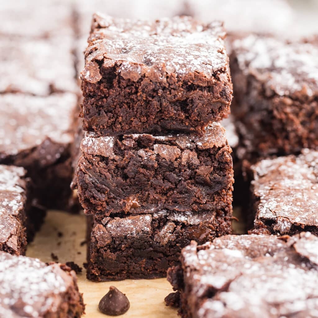 Square image of stacked brownies surrounded by more brownie pieces.