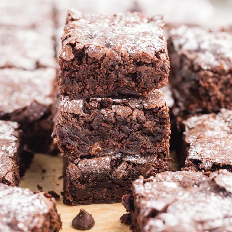 Square image of stacked brownies surrounded by more brownie pieces.