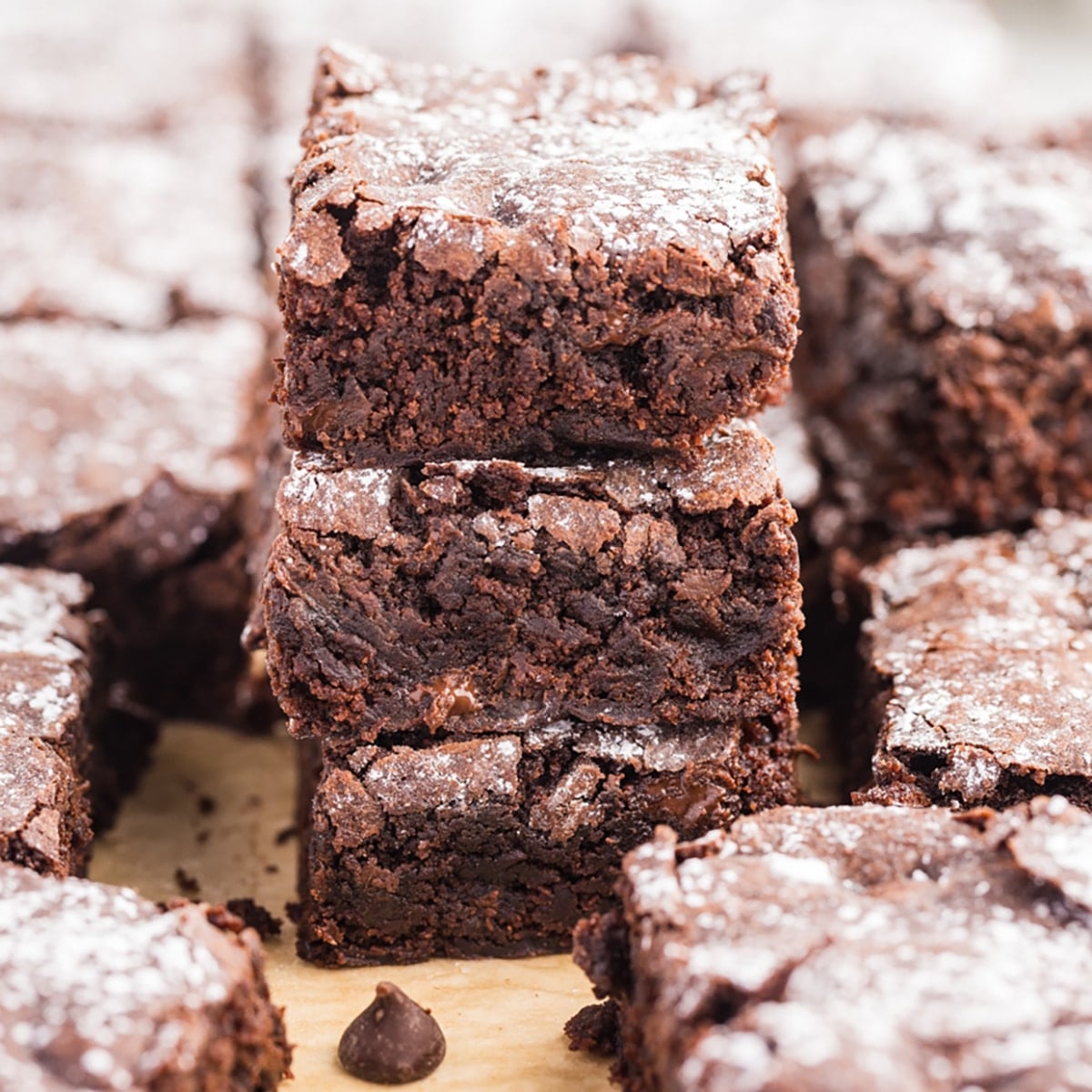 Square image of stacked brownies surrounded by more brownie pieces.