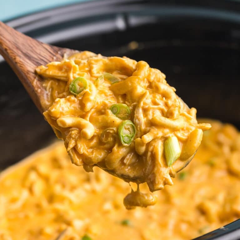 Wooden spoon lifting creamy buffalo chicken mac and cheese from slow cooker.