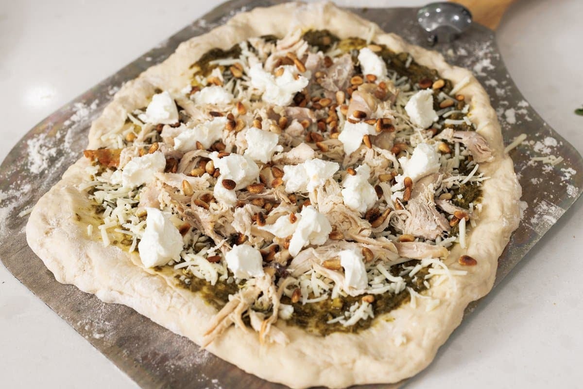 Pesto pizza topped with shredded chicken and goat cheese.