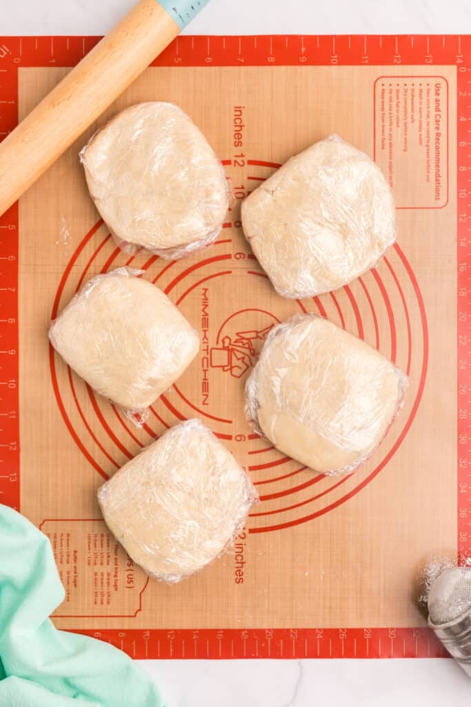 Five plastic-wrapped dough discs arranged on a pastry mat.