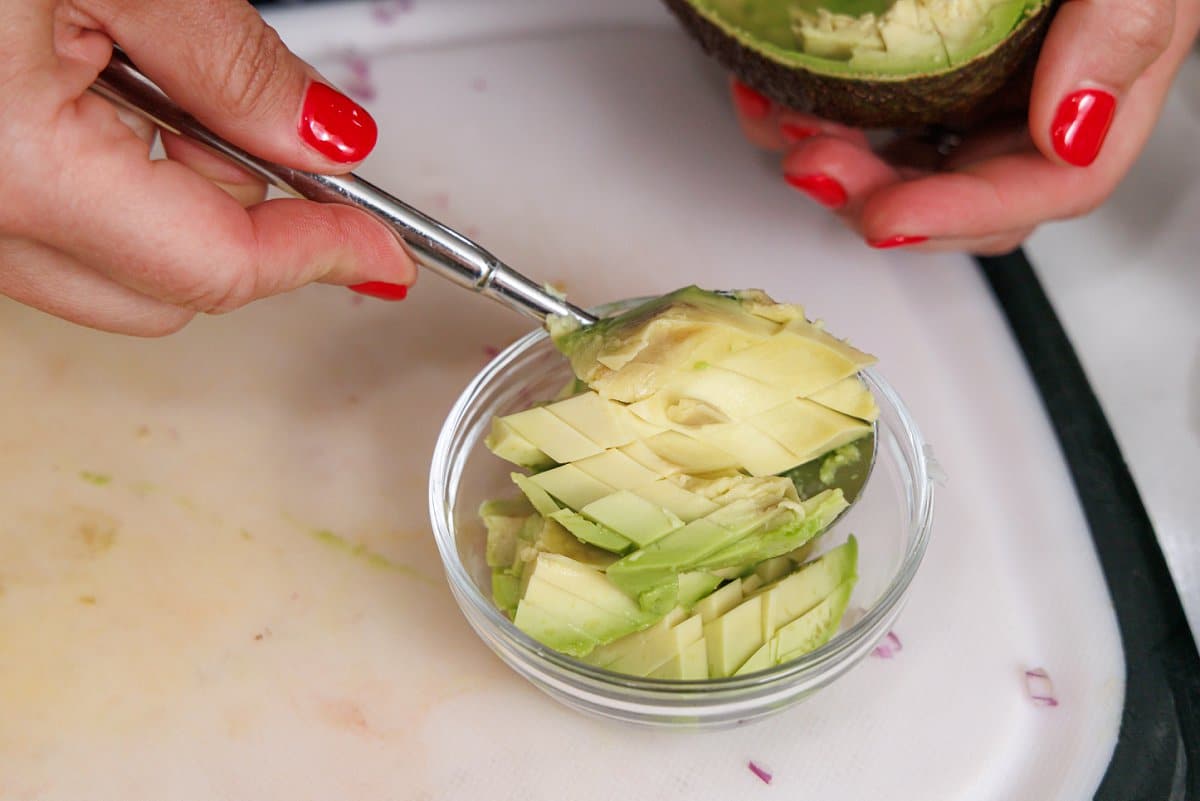 Scooping avocado into a small glass bowl.