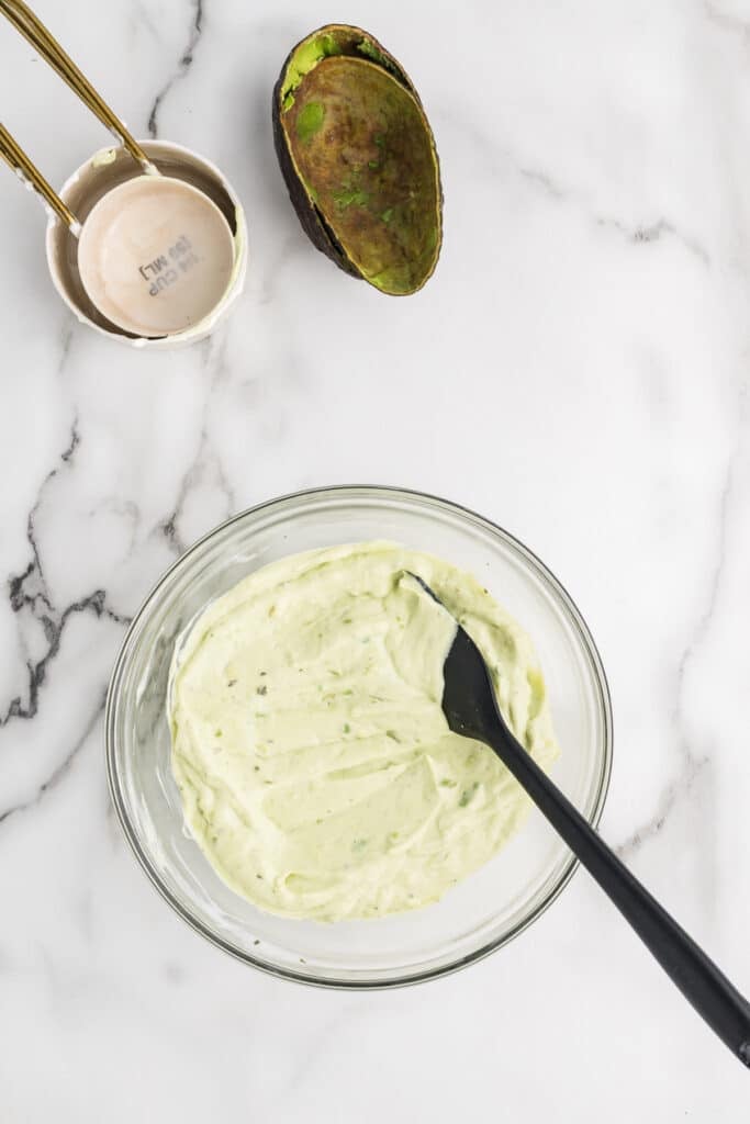 Green avocado dipping sauce in a bowl with a black spoon.