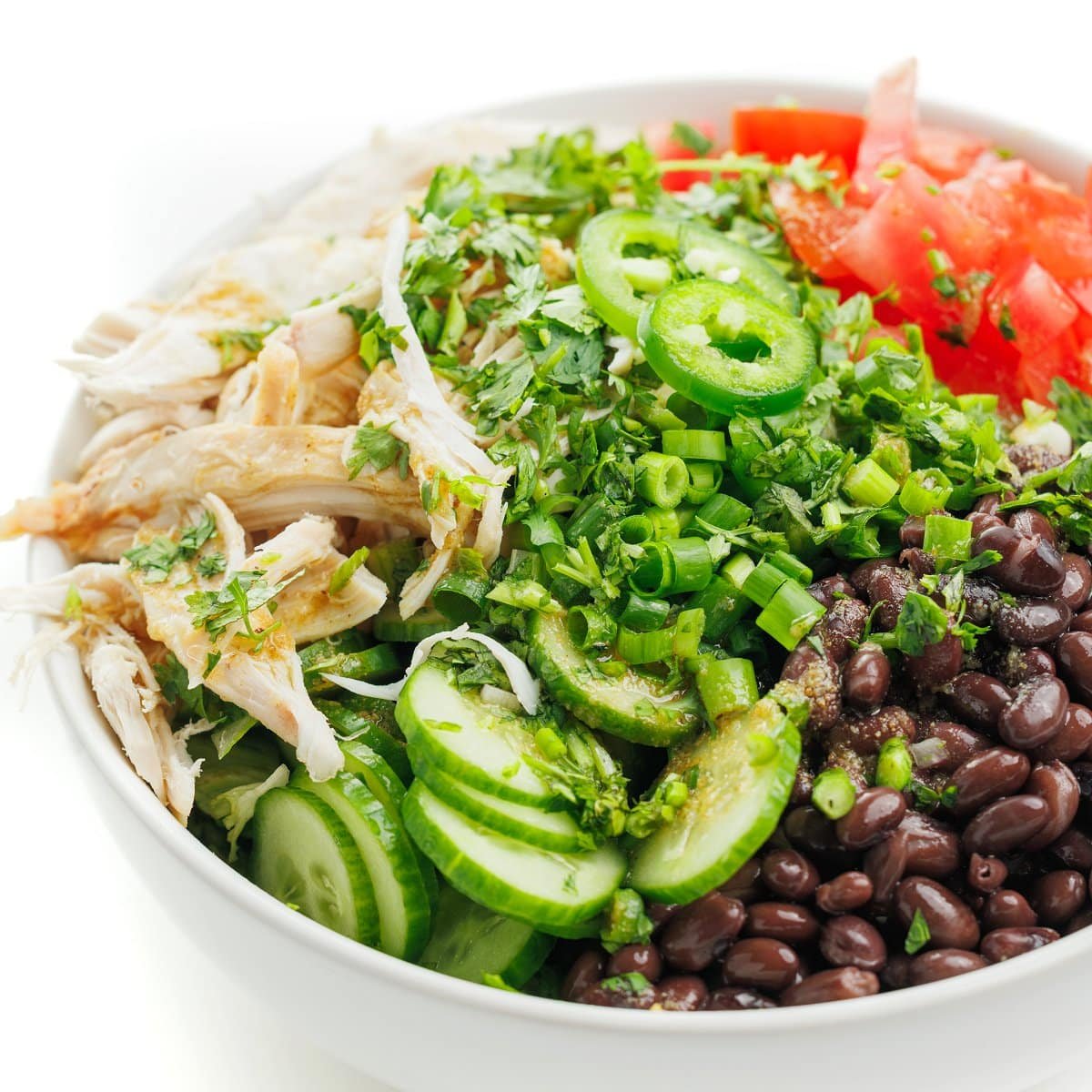 Chicken and black bean salad in a white bowl topped with jalapeños.