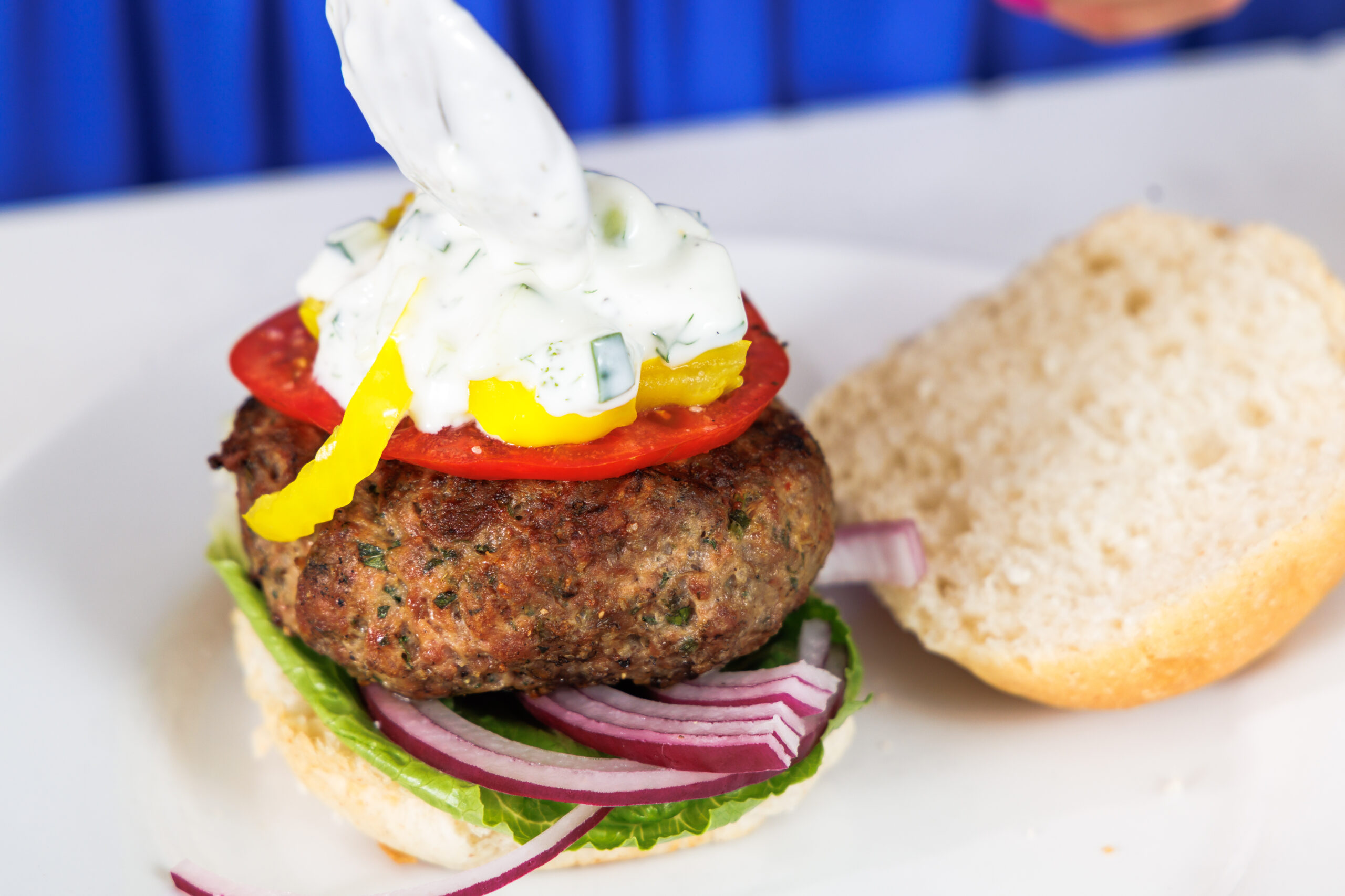Putting tzatziki sauce on top of greek lamb burger.