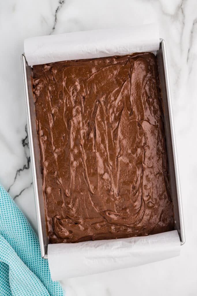 Pan of chocolate brownie batter lined with parchment paper.