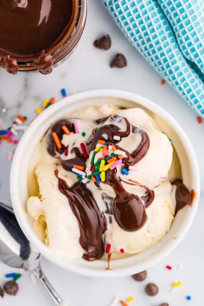 Vanilla ice cream topped with hot fudge and colorful sprinkles in a white bowl.