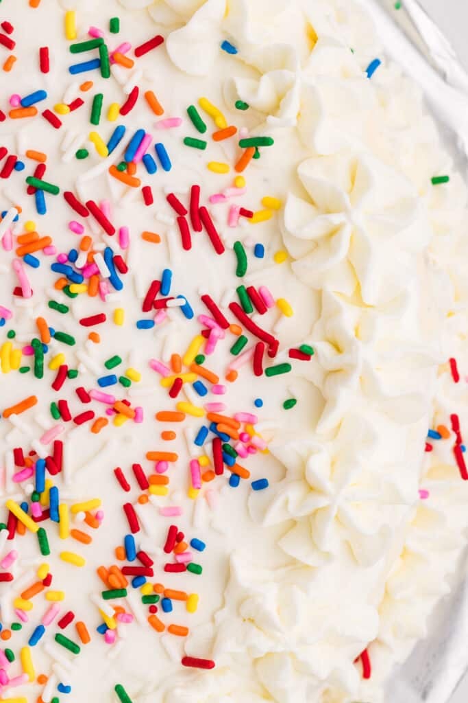 Close-up of white frosted cake topped with colorful rainbow sprinkles and piped frosting swirls.