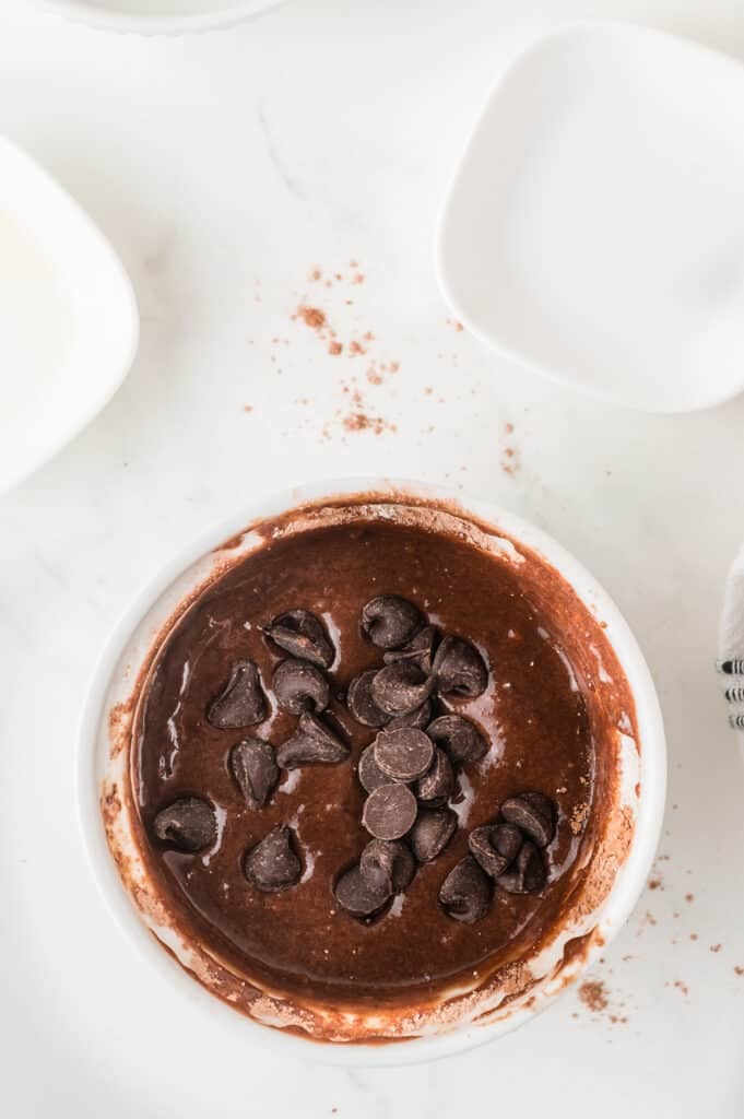 Unbaked brownie batter topped with chocolate chips in a white ramekin.