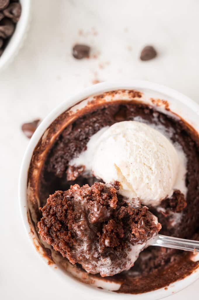 Freshly baked single serve brownie in a white ramekin topped with a scoop of melting vanilla ice cream.