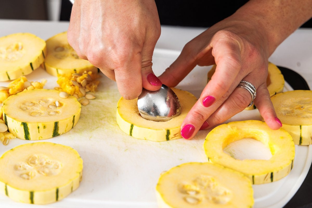 Using a spoon to cut the seeds out of the center of a delicata squash.