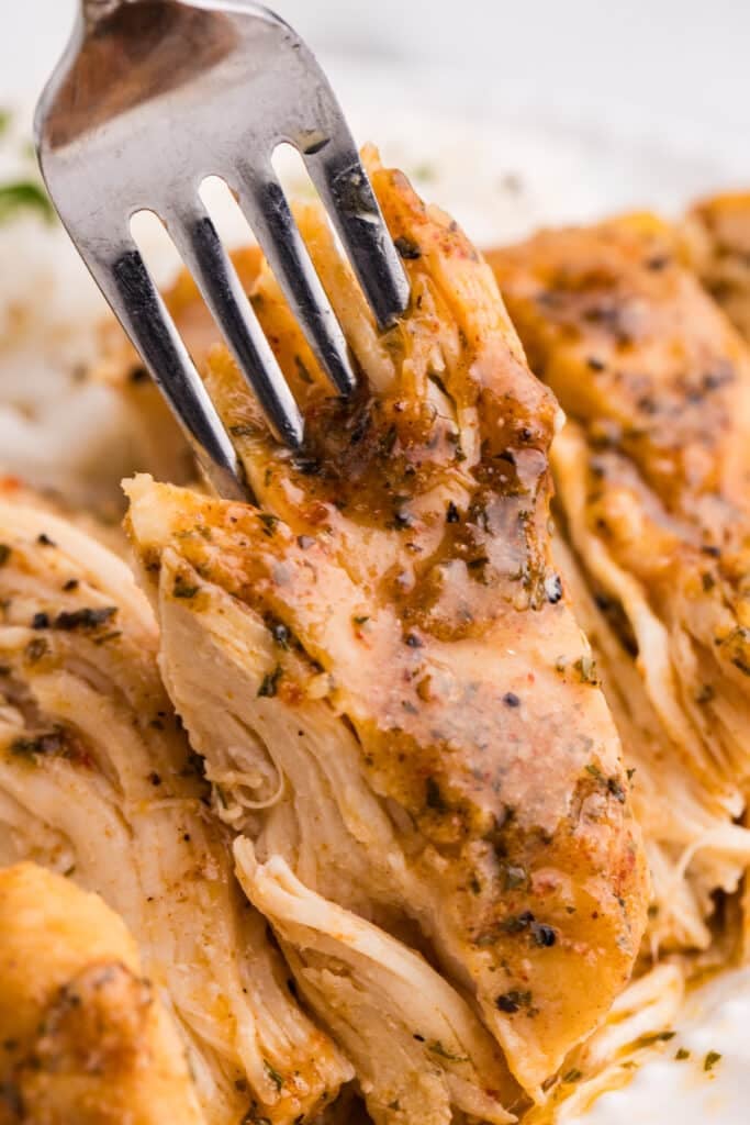 Close-up of a fork pulling apart tender, seasoned chicken breast.