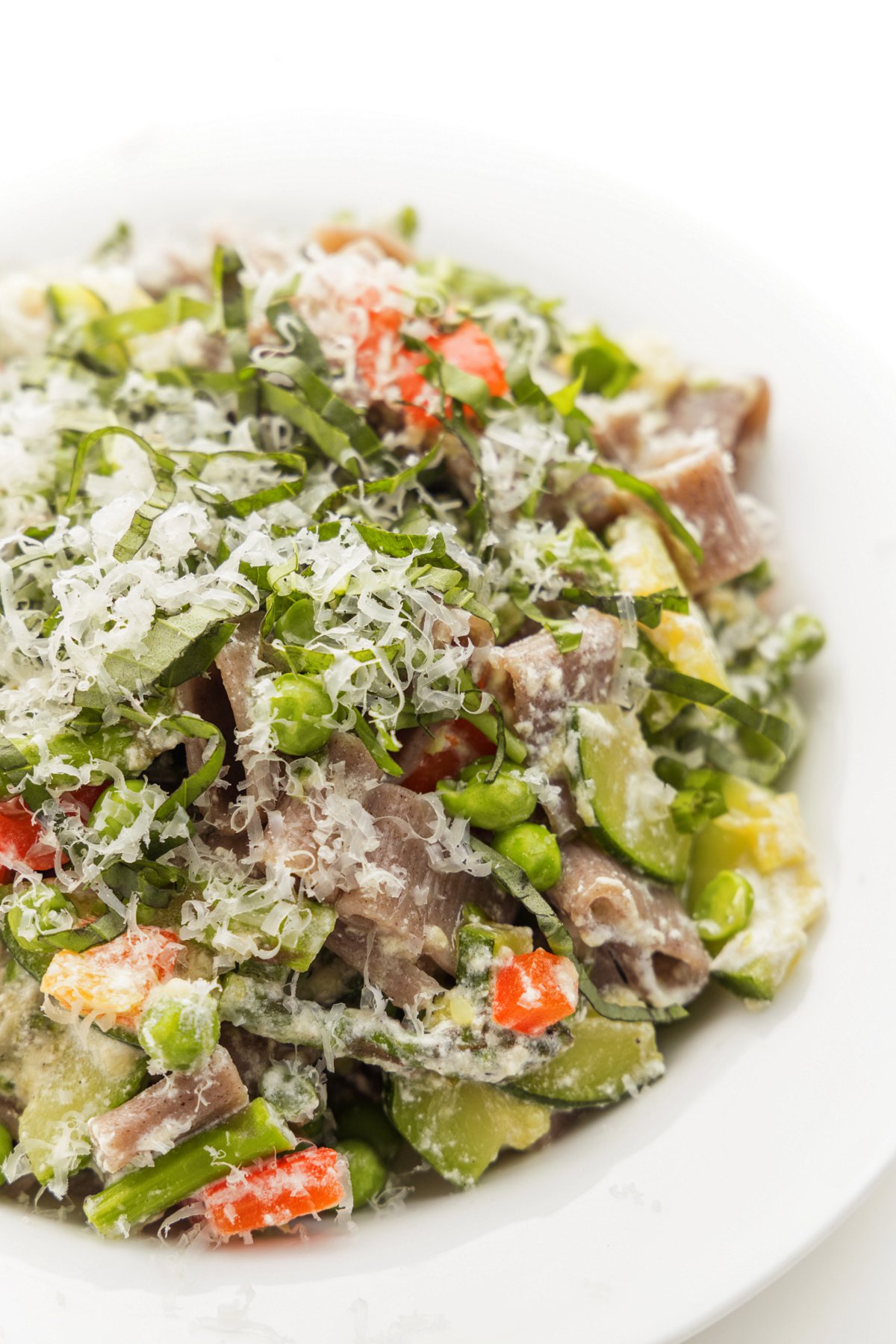 Primavera pasta with sautéed vegetables topped with freshly grated parmesan cheese and basil ribbons.