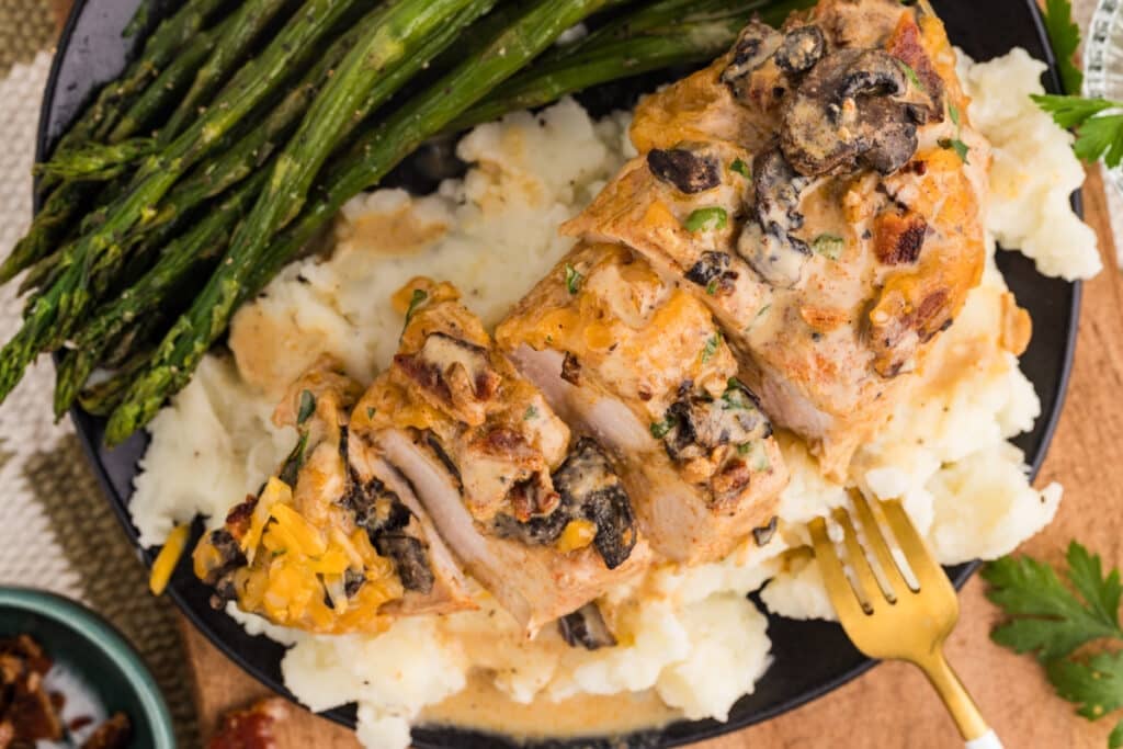 Sliced Alice Springs Chicken served over mashed potatoes with asparagus.