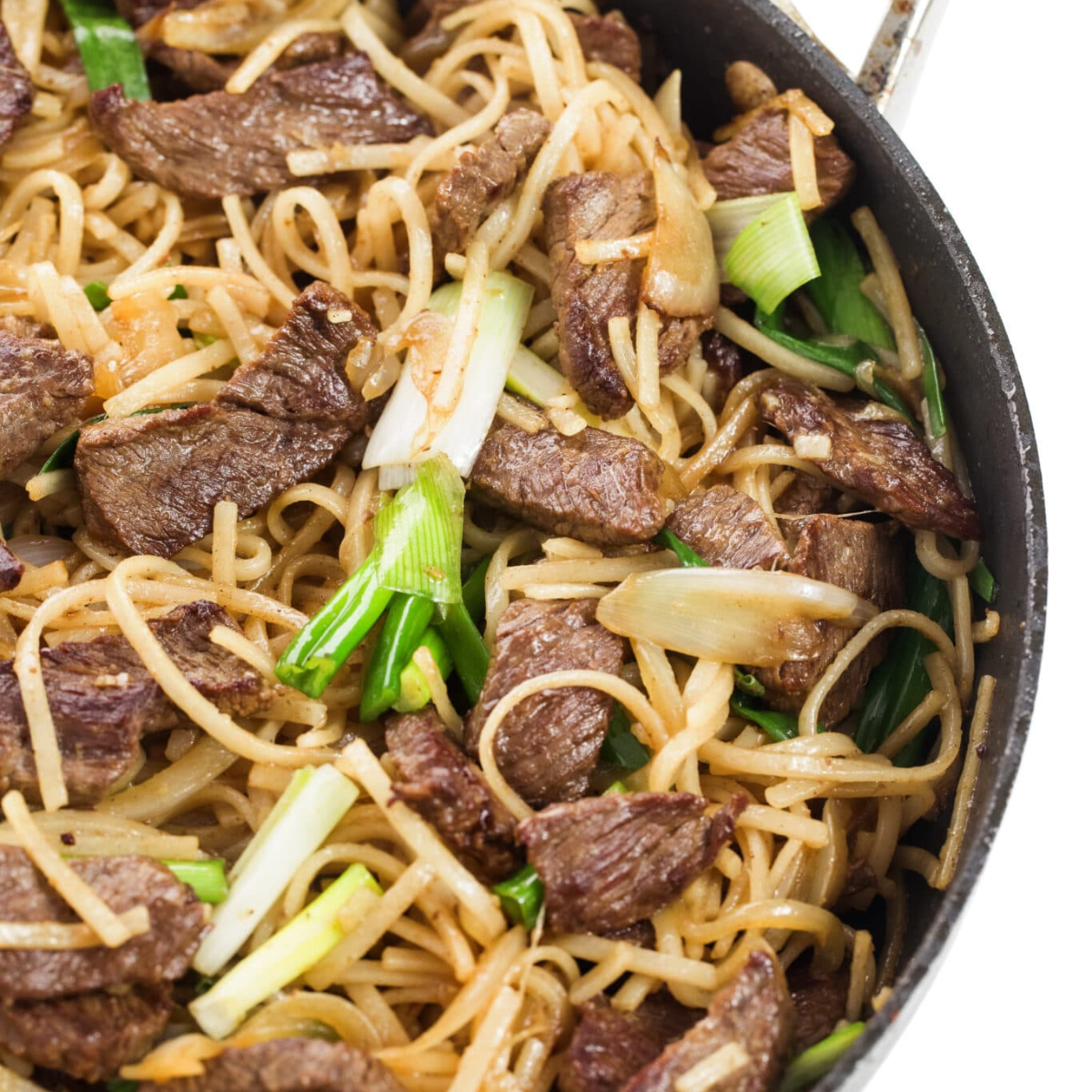 Beef stir-fry with rice noodles in a skillet with green onion.