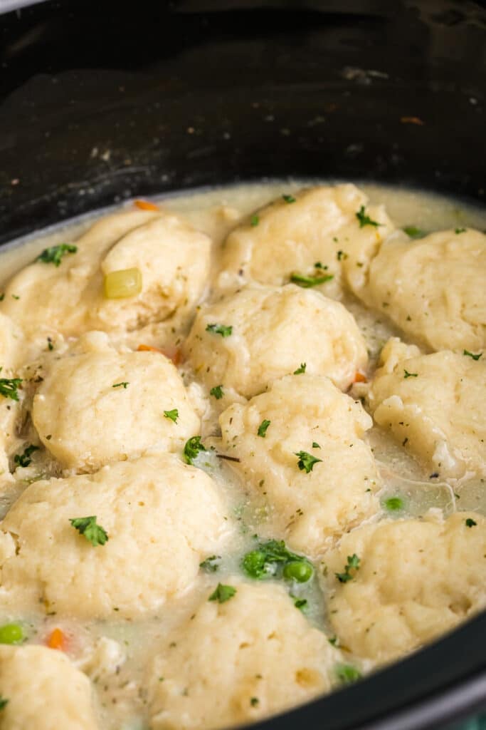 Fluffy dumplings cooking in a creamy broth topped with parsley.