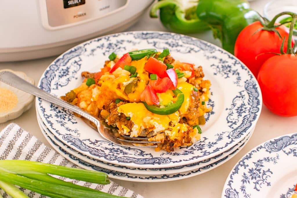 A plated serving of cheesy tater tot casserole topped with diced tomatoes and sliced jalapeños.