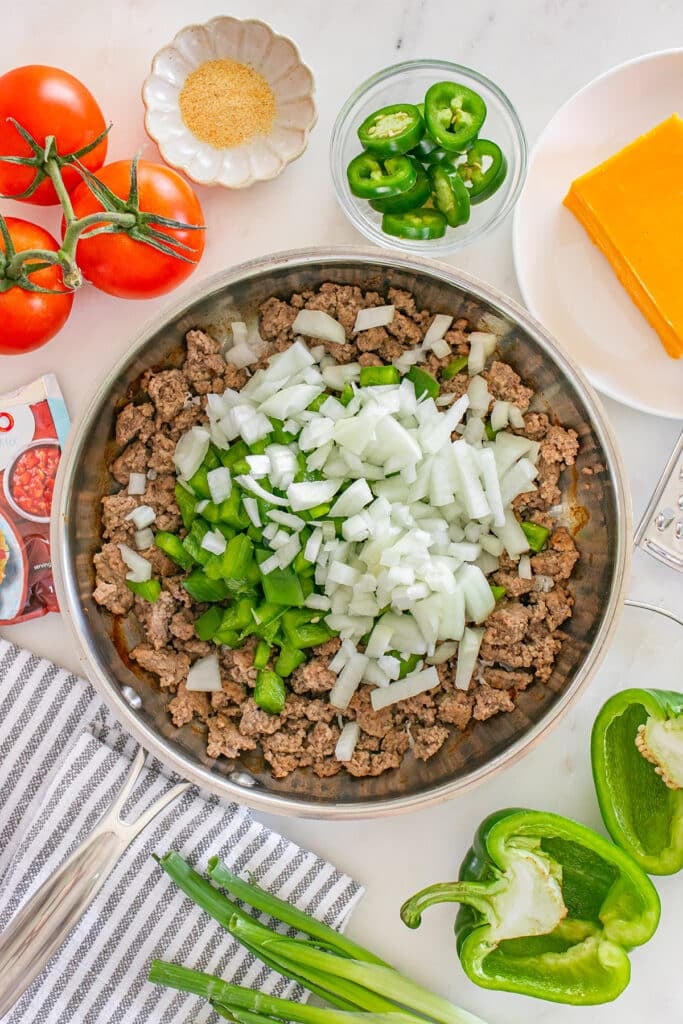Ground beef in a skillet topped with chopped onions and green bell peppers.