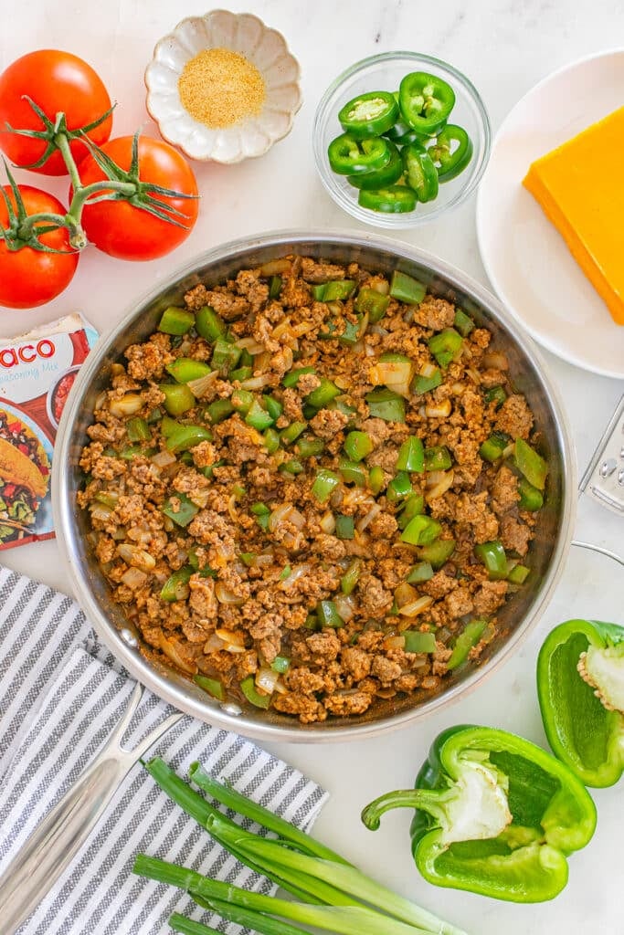 A skillet filled with cooked ground beef, onions, and green bell peppers.