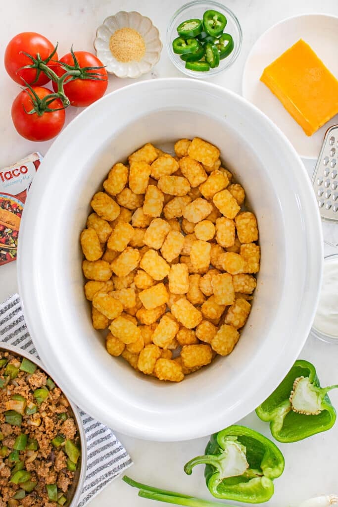 A slow cooker filled with a full layer of golden tater tots.