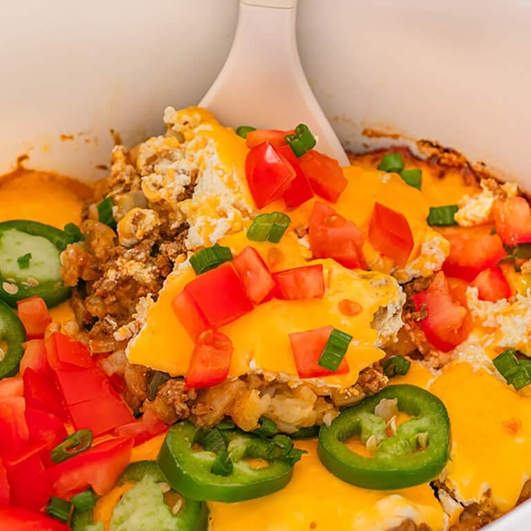 Close-up of a cheesy casserole topped with diced tomatoes and sliced jalapeรฑos.