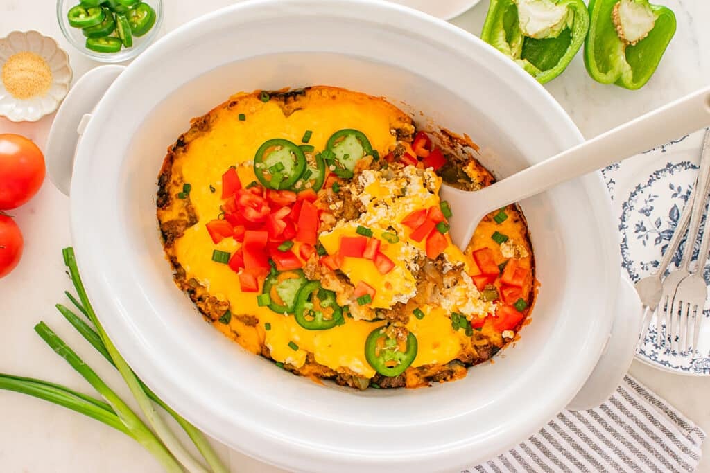 Cheesy casserole inside a slow cooker topped with tomatoes and jalapeños.