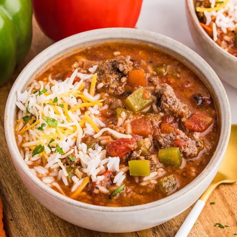 A bowl of stuffed pepper soup topped with shredded cheese and rice.