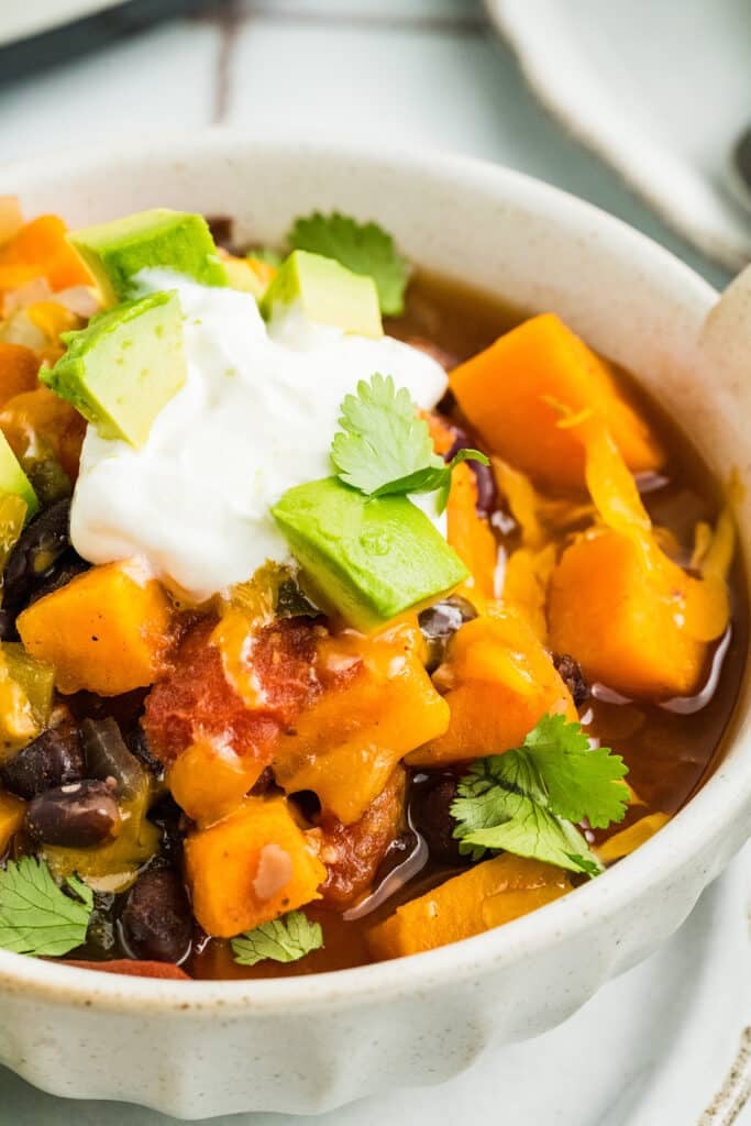 A bowl of chili topped with avocado chunks, sour cream, and cilantro.