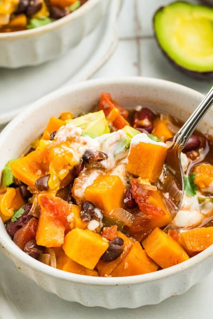 A bowl of chili filled with sweet potatoes, black beans, tomatoes, and avocado topped with sour cream.