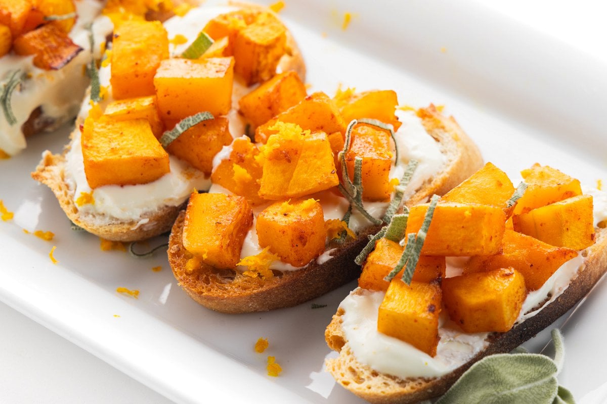Butternut squash crostini with whipped goat cheese and sage on a platter.