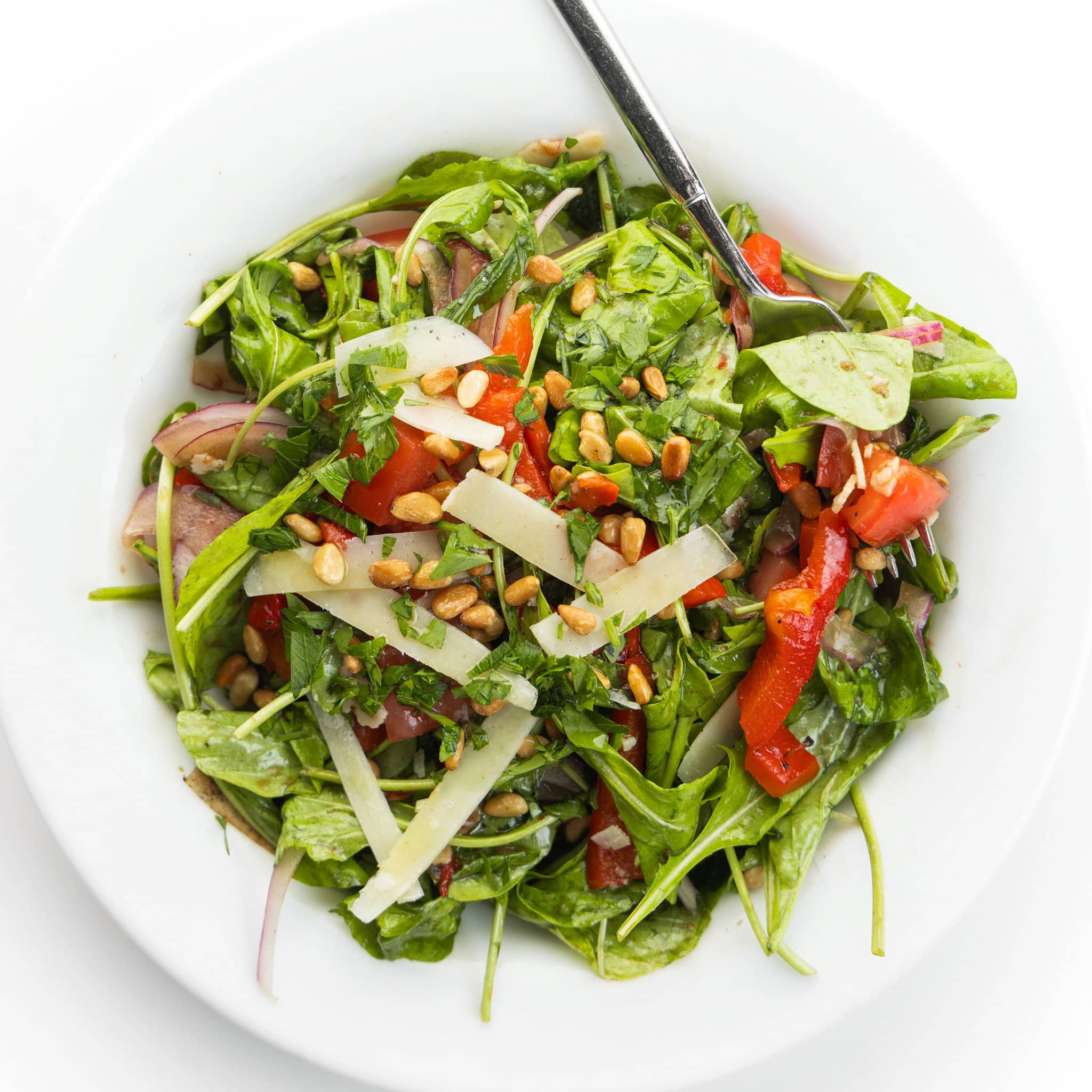 Italian mixed salad with shaved parm on a white plate with a fork.
