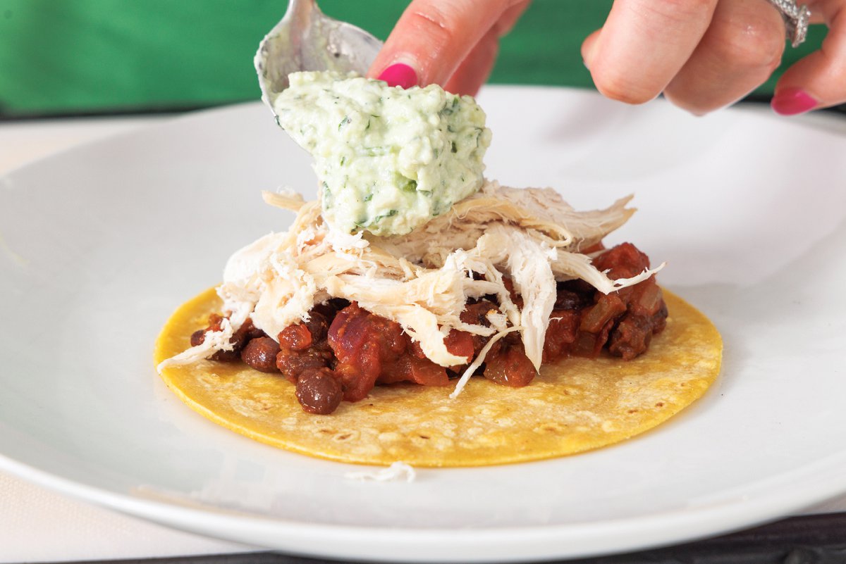 Assembling chicken and black bean taco on corn tortilla with a dollop of avocado crema.