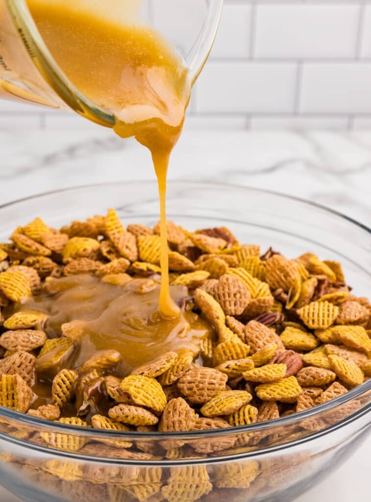 Caramel sauce being poured over cereal and pecans in a glass bowl.