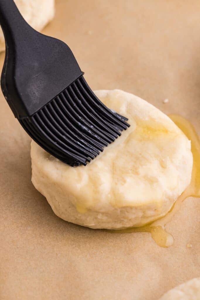 A pastry brush applying melted butter to an unbaked biscuit.