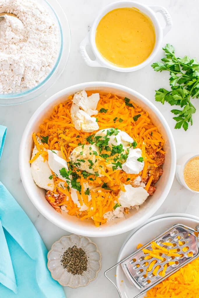 A mixing bowl filled with shredded cheese, cream cheese, and sausage mixture topped with parsley.