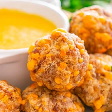 Close-up of golden sausage balls next to a bowl of yellow dipping sauce.