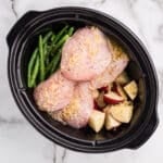 Raw chicken, red potatoes, and green beans in a slow cooker topped with minced garlic.