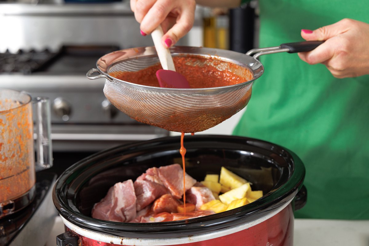 Straining sauce through a fine mesh strainer into a slow cooker.
