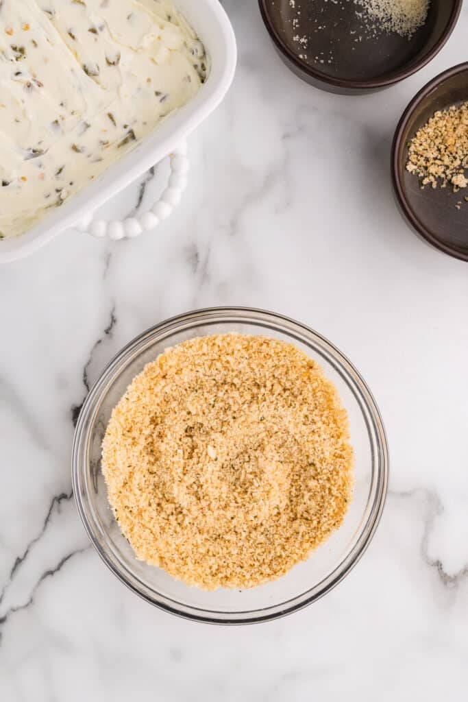 Breadcrumb topping in a glass bowl with dip ingredients nearby.