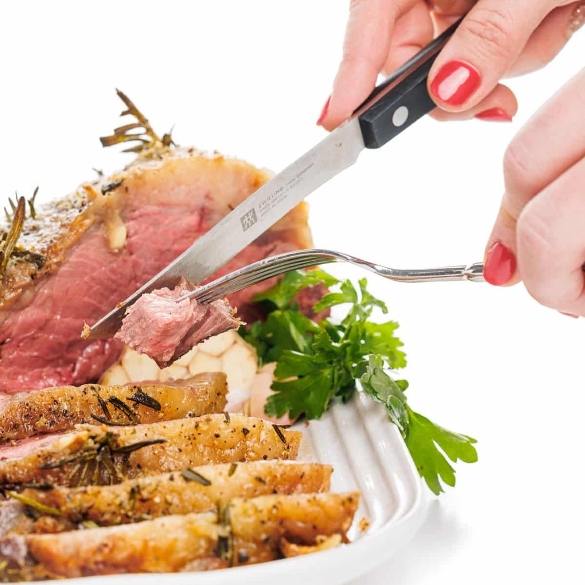 A fork stabbing a piece of garlic and rosemary studded beef roast with a knife.