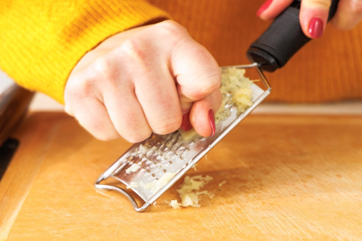 Grating fresh ginger onto a cutting board.