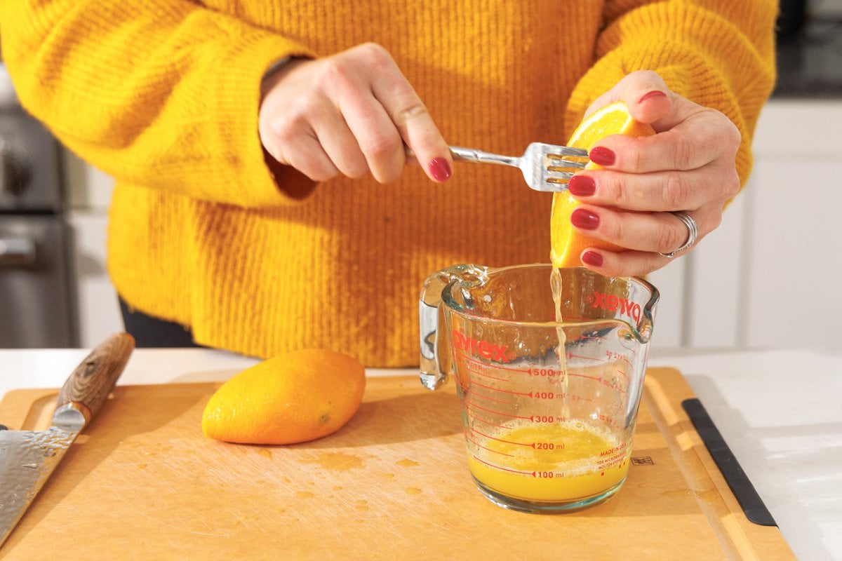 Using a fork to juice an orange into a liquid measuring cup.