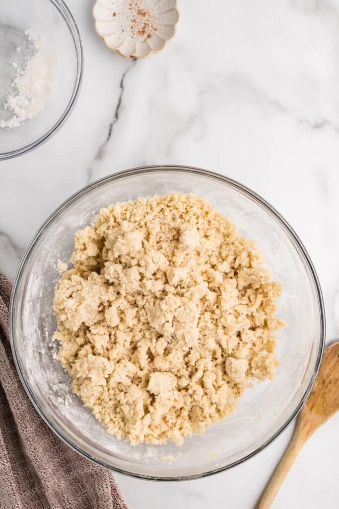 A glass bowl filled with crumbly cookie dough on a marble surface.