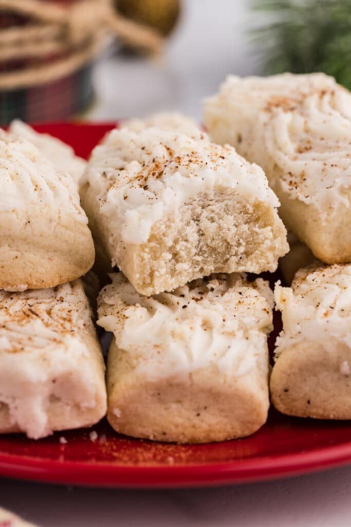 A frosted rectangular cookie with a bite taken out, stacked on a red plate.