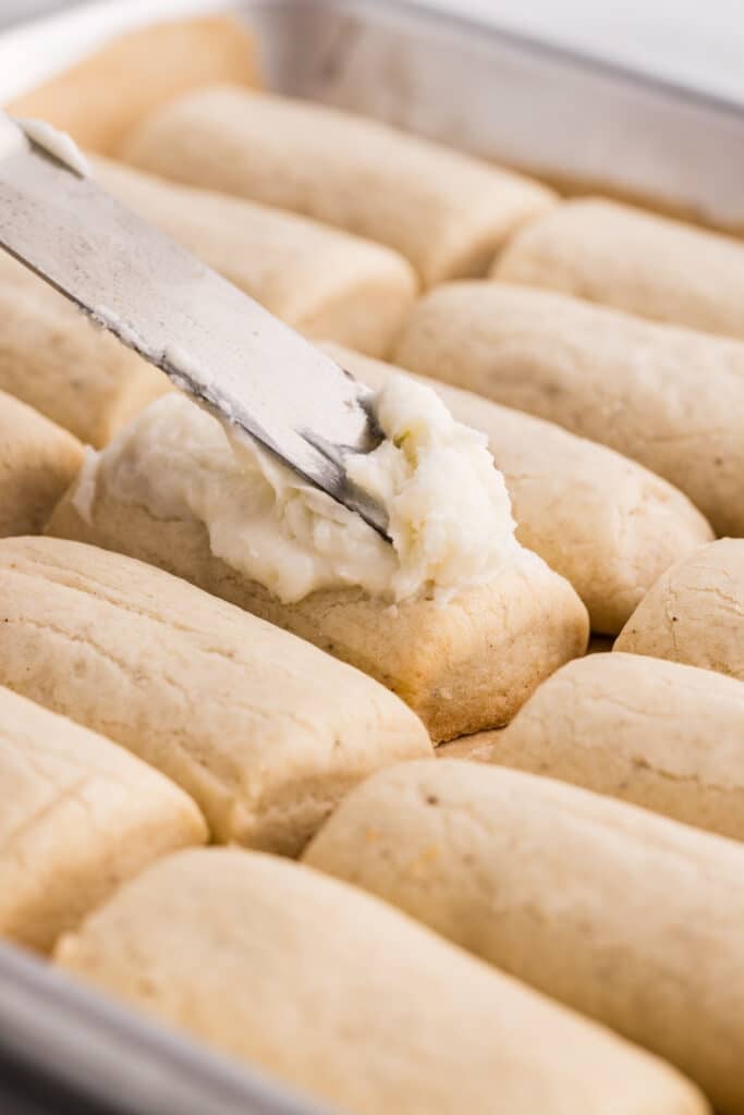A knife spreading white frosting onto a rectangular baked cookie.