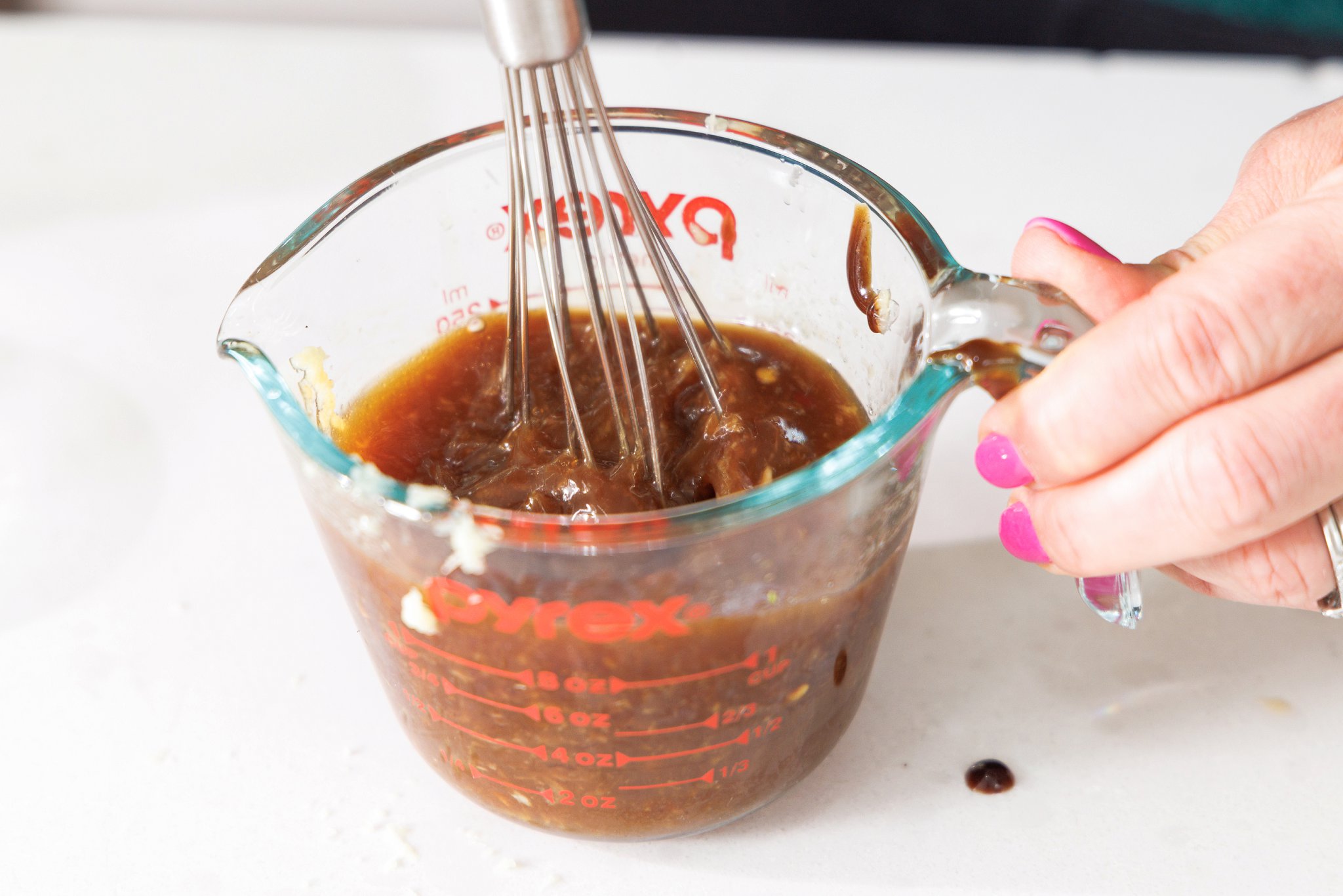Whisking ginger-garlic sauce in a liquid measuring cup.