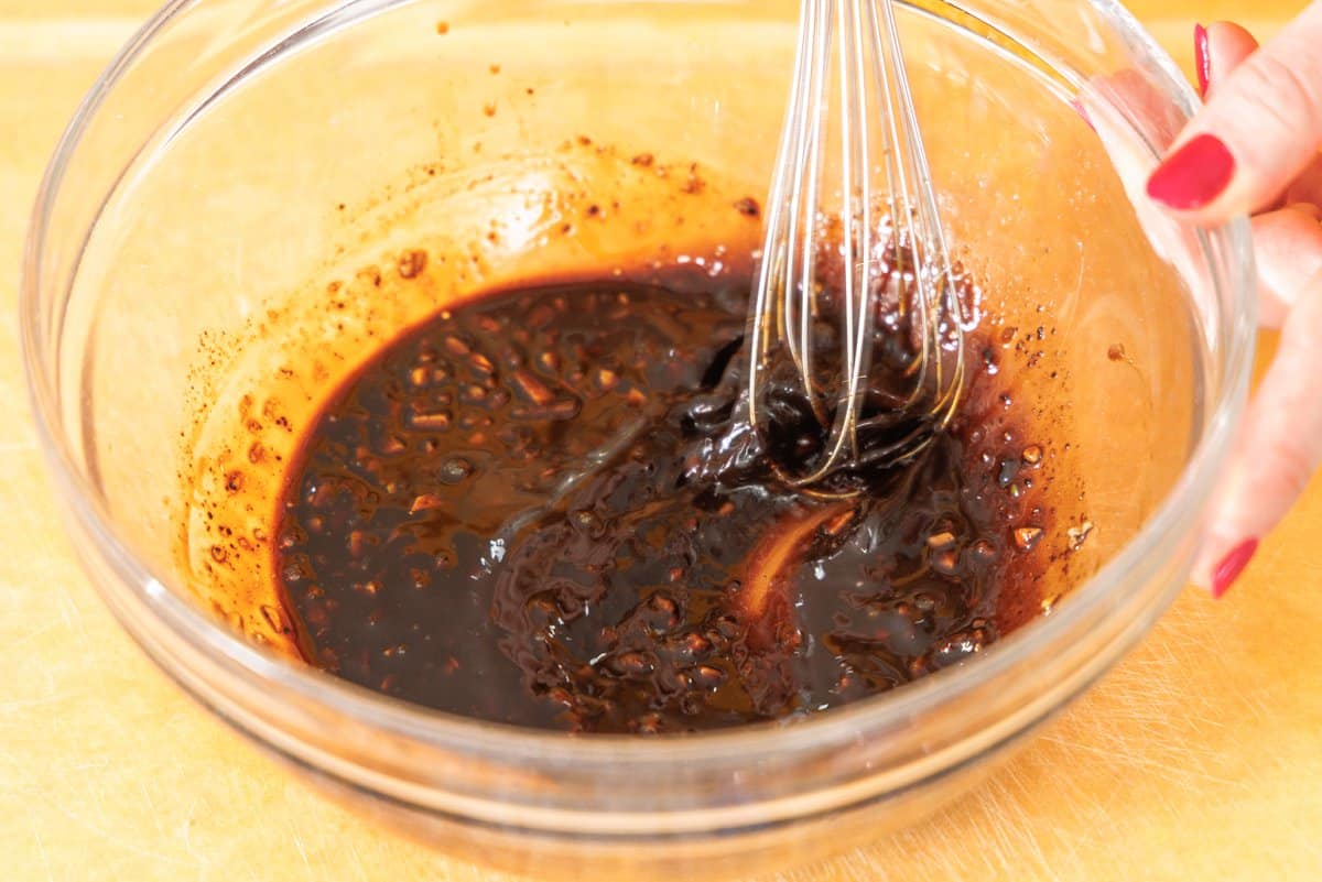 Whisking together tamarind lime vinaigrette in glass bowl.